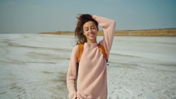 Mujer alegre en suéter acogedor con mochila naranja en el paisaje natural de los pisos de sal, se parece a un desierto blanco — Vídeos de Stock