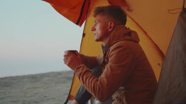 Adulto uomo escursionista seduto all'ingresso tenda e tenendo tazza con caffè in mano — Video Stock