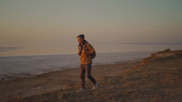 Sırt çantalı bir gezgin terk edilmiş deniz sahilinde gün doğumuyla buluşuyor. — Stok video
