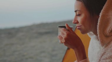 Kendine güvenen güzel bir kadının portresi çadırın girişinde oturuyor ve elinde kahveyle bardağı tutuyor..