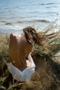 Güzel çıplak vücutlu, deniz kenarında poz veren bir kadın.