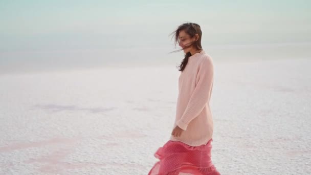 Caminante chica en suéter grande y soplado vestido rosa en el hermoso paisaje de pisos de sal en el lago rosa — Vídeos de Stock