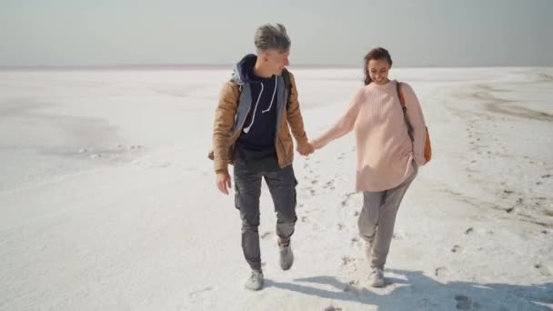 Mutlu çift gezginler pembe beyaz tuzlu sahilde el ele yürüyor — Stok video