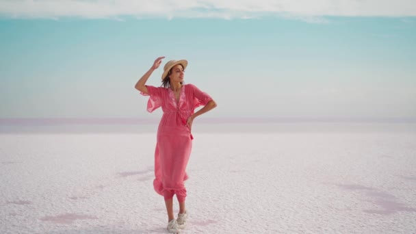 Gelukkig zorgeloze elegante vrouw in blazen roze jurk en stro hoed poseren op witte zoute verlaten strand — Stockvideo