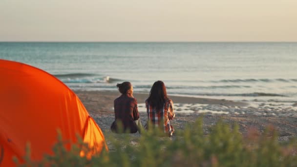 Bakre vy kvinnligt par sitter vid soluppgången på stranden framför havet — Stockvideo