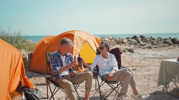 Hermosa mujer en camisa blanca y hombre guapo en camisa casual y jeans bebiendo cerveza fría en el día soleado caliente en acampar — Vídeo de stock