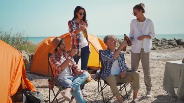 Grupp vänner resenärer koppla av i lägerstolar vid tält i camping på havskusten — Stockvideo