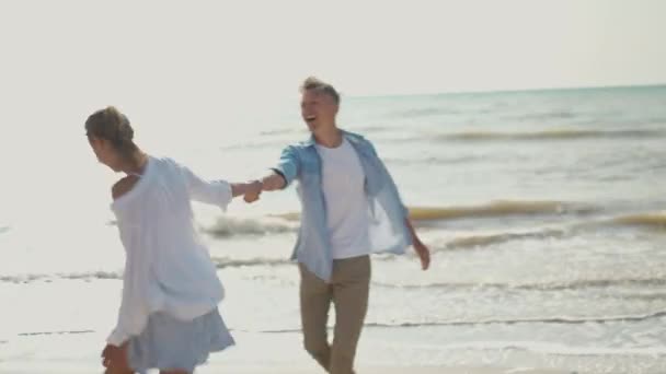 Alegre lindo casal se divertindo correndo ao longo da praia de areia juntos — Vídeo de Stock