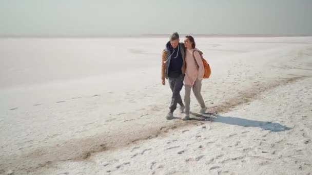 Gelukkig glimlachen mooie paar reizigers lopen knuffelen elkaar op verlaten roze witte zoute kust — Stockvideo