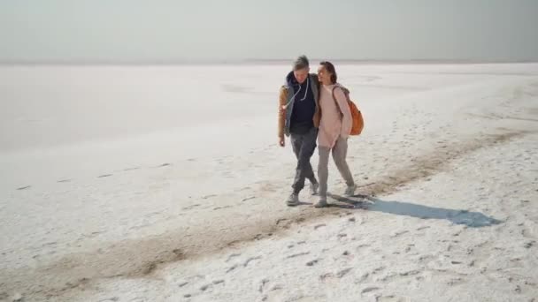 Happy smiling lovely couple travelers walking hugging each other on deserted pink white salty coast — Stock Video