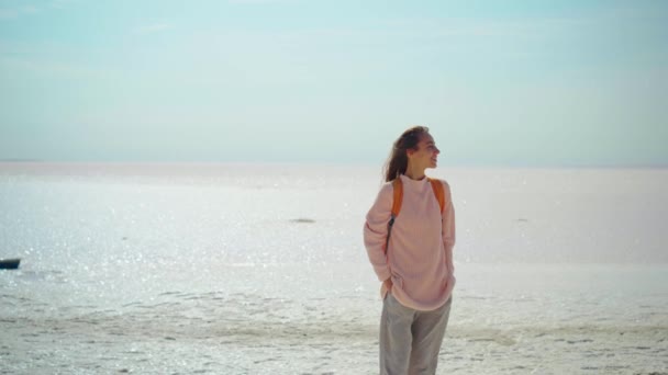 Mujer alegre en suéter acogedor con mochila naranja en el paisaje natural de los pisos de sal, se parece a un desierto blanco — Vídeos de Stock