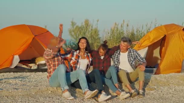 Fyra bästa vänner sitter vid solnedgången på stranden framför havet och tillbaka till orange tält — Stockvideo