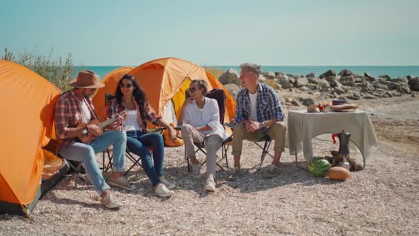 Picnic of young adult people and ukulele on beach with tents — Stock Video