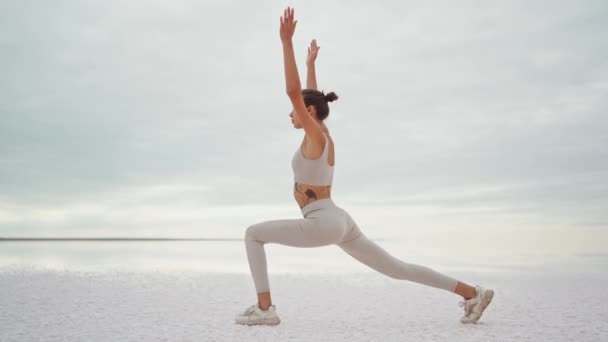 Vista posteriore giovane attraente donna in forma che esegue una posa yoga all'alba sulla costa secca del lago salato al mattino nuvoloso. — Video Stock