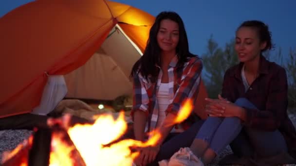 Due belle ragazze sedute al falò vicino alla tenda arancione aperta — Video Stock