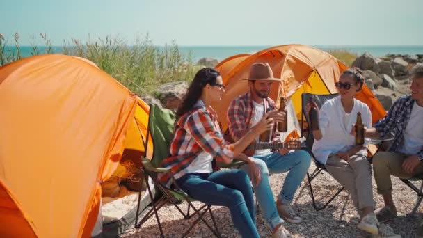 Groep gelukkige vrienden drinken bier en plezier hebben op het strand samen. volwassen reizigers toasten bier en genieten samen op de camping aan zee — Stockvideo
