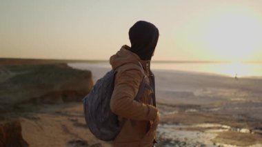 Orta yaşlı bir gezgin gün doğumunda deniz kıyısına bakıyor.