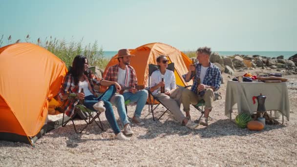 Група дорослих радісних друзів, які розслабляються в кріслах, п'ють пиво і розважаються на пляжі разом — стокове відео