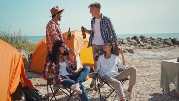 Fyra vuxna vänner resenärer njuter av sommarsemester och dricka kall öl på varm solig dag i camping på havskusten — Stockvideo