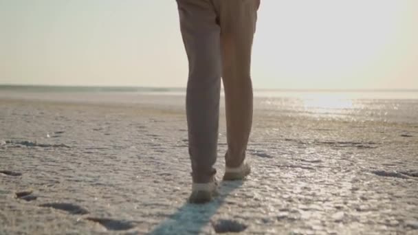 Ralenti vue arrière femmes pieds et dos, fille randonneur marchant le long de la plage blanche avec des flocons de sel cristallisé sur la côte du lac de sel minéral — Video