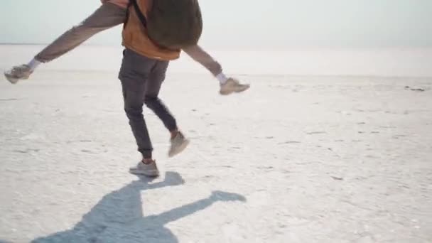 幸せな陽気な魅力的な女性は男にジャンプし、抱擁し、彼にキス。砂漠の自然塩のフラットで屋外で幸せなカップルハイカー — ストック動画