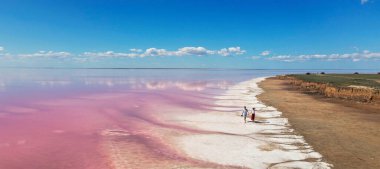 Pembe gölün beyaz, tuzlu kıyılarında yürüyen panoramik çift.