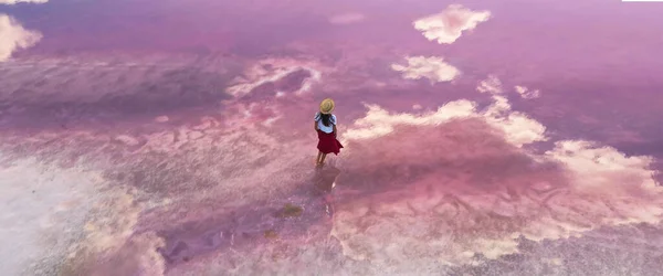 Pembe gölün sularında yürüyen, sakin yüzeyi ve yansımaları olan hava manzaralı kız..