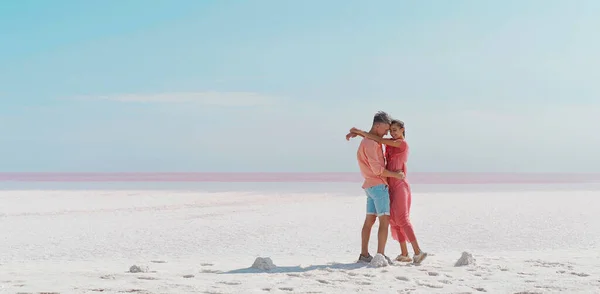 Vakkert par som omfavner hverandre på vindfull, salt kyst på rosa saltsjø – stockfoto