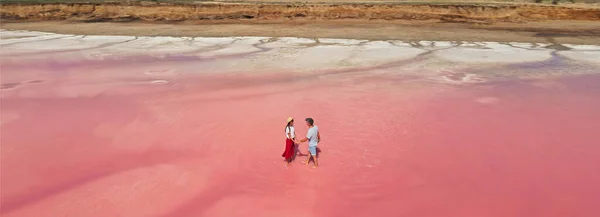 Aerial epic drone image couple standing in bright pink water of lake with salty coast Stock Picture