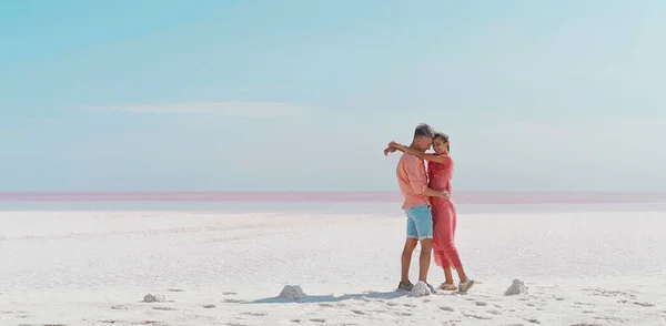 Vakkert par som omfavner hverandre på vindfull, salt kyst på rosa saltsjø stockbilde