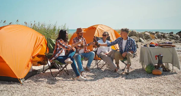 Group adult joyful friends relaxing in capm chairs, drinking beer and having fun at beach together Stock Image