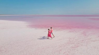 Güzel romantik bir çiftin hava destansı görüntüsü. Beyaz tuzlu sahilli, mineral gölünün parlak pembe sularında yürüyor.