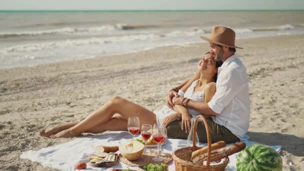 Familia joven cariñosa pareja feliz marido y esposa sentarse en acogedora manta de picnic con vino, frutas, cesta con pan. — Vídeos de Stock