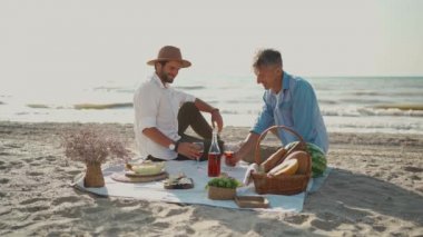 Avrupalı mutlu eşcinsel çift şarap içiyor ve sahilde romantik pikniğin tadını çıkarıyor..
