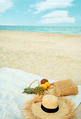 Yazın plaj aksesuarları ve kumlu sahilde mavi deniz ve gökyüzüne karşı taze meyve.