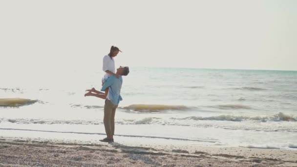 Piękny szczęśliwy para mężczyzna i kobieta ambracing na plaży nad morzem i mężczyzna kładzie jego dziewczyna na ręce pocałunek. — Wideo stockowe