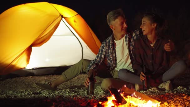 Schönes Paar, das nachts neben dem Feuer auf dem Campingplatz ausharrt — Stockvideo