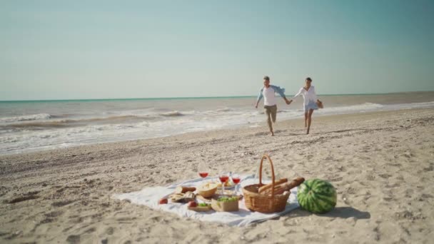 Câmara lenta casal feliz em piquenique na praia. pessoas alegres correndo ao longo de Sandy Beach — Vídeo de Stock