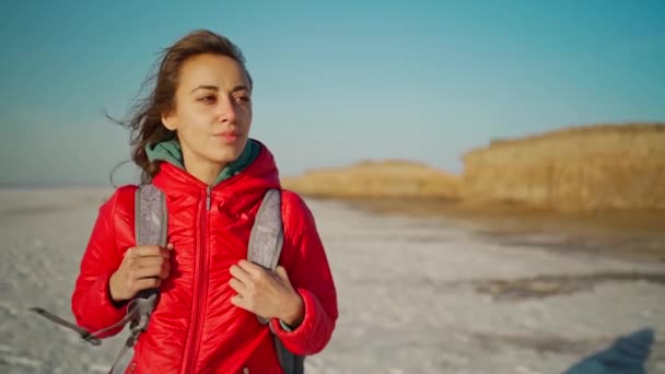 Lassú mozgás portré vonzó magabiztos és nyugodt fiatal nő túrázó piros kabátban séta sós tó partján — Stock videók