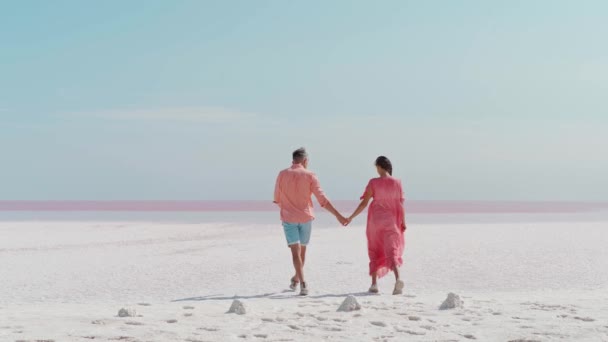 Стильная элегантная пара прогуливаясь по белому соленому побережью выглядит как пустыня, отпуск медового месяца — стоковое видео