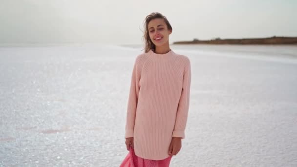 Macchina fotografica tenuto in mano riprese bella donna in maglione kozy e abito rosa a piedi sulla costa salmastra ventosa sul lago salato rosa — Video Stock