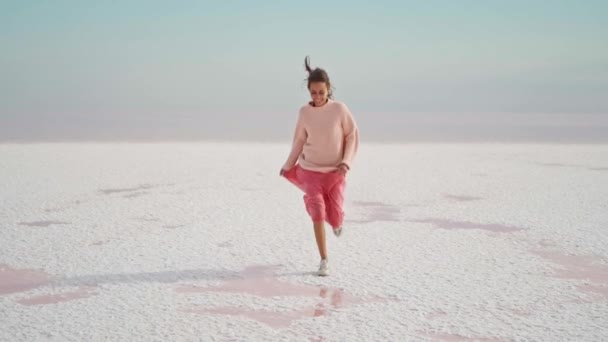 분홍색 옷을 입은 행복 한 여성 이 하얀 사막 지역의 무기물로 덮인 분홍색 호수 위를 카메라로 달리고 있다. — 비디오