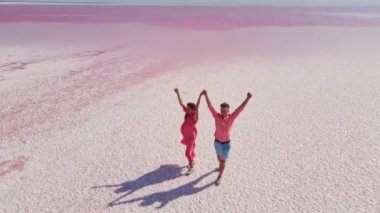 Mutlu çiftin, mineral gölünün parlak pembe sularında yürüyüp eğlenirken çekilmiş hava aracı görüntüleri..