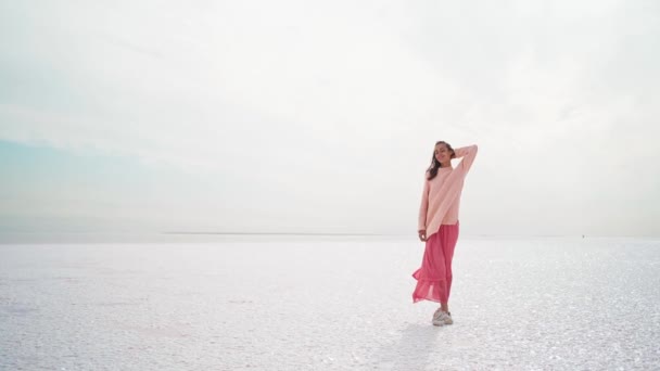 Wunderbare verträumte Frau in dickem Pullover und rosa Kleid posiert an windiger Salzküste am rosa Salzsee. — Stockvideo