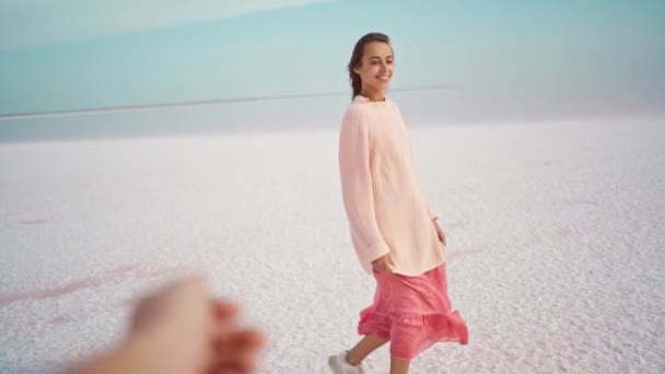POV πρώτο πρόσωπο δείτε όμορφη ευτυχισμένη γυναίκα σε μεγάλο άνετο πουλόβερ και ροζ φόρεμα με τα πόδια σε θυελλώδη αλμυρή ακτογραμμή σε ροζ αλμυρή λίμνη. — Αρχείο Βίντεο