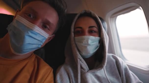Boldog pár férfi és nő orvosi biztonsági maszkban a repülőgép kunyhóban az ablak mellett a felszállásra. az emberek élvezik az utazást és a járatok lehetőségét karantén után — Stock videók