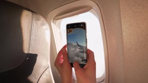 Close up mobile phone in female hands filming aircraft wing through window. woman enjoying view from plane and shoots video by phone during take off. — Stock Video