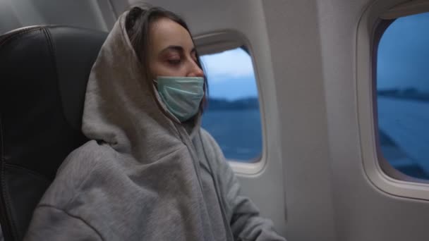 Donna con cappuccio e maschera medica nella cabina dell'aeroplano. voli aerei e di viaggio durante la pandemia e la quarantena di Covid-19. — Video Stock