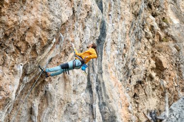 Bir adam yüksek kayalıklarda dinleniyor, zor bir yola odaklanmış.