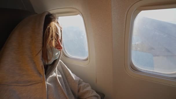 Müde Passagierin mit Gesichtsmaske schläft im Sitz am Fenster im Flugzeug — Stockvideo